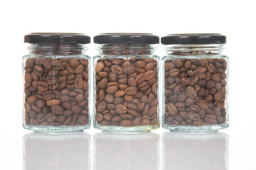 three glass jars with black lids filled with roasted coffee beans arranged in a row on a reflective...