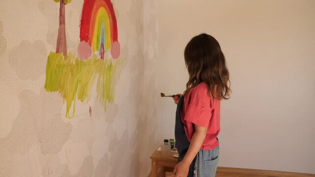 Young artist painting rainbow on wall with brush and tempera colors
