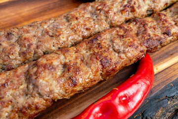 Delicious skewers of grilled meat with vibrant red chili resting on a wooden board