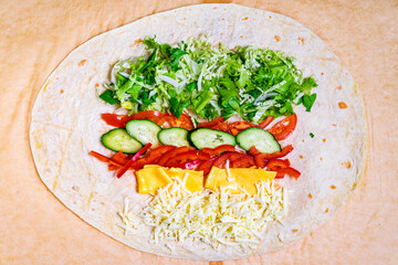Colorful wrap being prepared with fresh vegetables and cheese on a tortilla at a kitchen counter