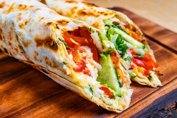 Freshly made wrap filled with vegetables and grilled chicken served on a wooden board in a casual dining setting