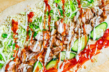 Delicious wrap being prepared with grilled chicken, fresh vegetables, and flavorful sauces on a wooden surface