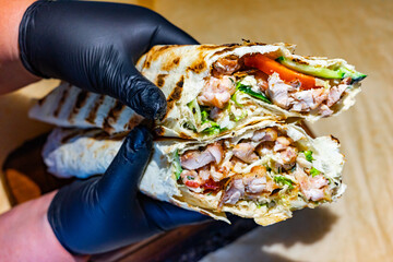 Delicious grilled chicken wraps being held by hands with gloves in a casual dining setting