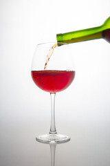 Close-up of a green wine bottle filling a crystal wine glass with deep red wine, showcasing bubbles and flow. Minimalist white backdrop enhances the elegance, great for alcohol brands