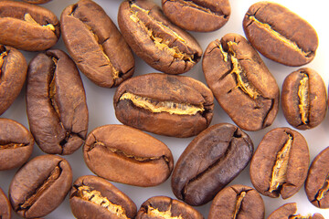 Close-up of roasted coffee beans with rich brown hues, showcasing their textured surfaces and natural splits on a white background. Perfect for coffee-related themes.