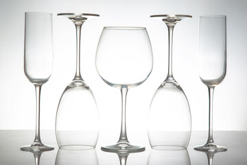 A sleek lineup of five elegant, empty wine glasses with long stems, reflecting on a glossy surface against a soft gray background, perfect for dining or event themes.