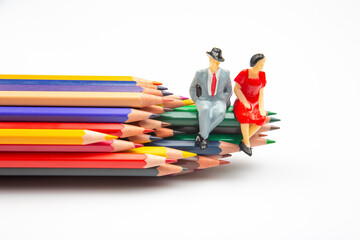 Colorful pencils spread across a white surface, with miniature businessmen standing, merging...