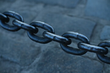 A thick metal anchor chain against a background of cobblestones