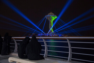 Women in traditional dress watch a spectacular light show at the Al-Khobar water tower