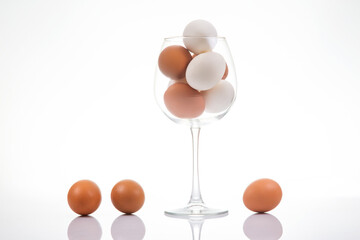 A wine glass filled with white and brown eggs, with three eggs placed beside it on a reflective...