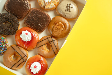 A variety of colorful donuts arranged in a box, featuring a mix of glazed, chocolate-coated, and sprinkled toppings. The assortment includes donuts with vibrant green, white, red, and chocolate