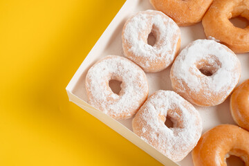 A variety of colorful donuts arranged in a box, featuring a mixture of glaze, and powdered sugar....