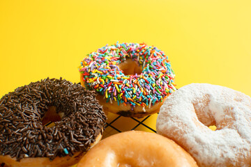 A close-up shot of a variety of donuts on a cooling rack. The donuts are topped with colorful sprinkles, pink stripes, glazed, almond, cream. Perfect for recipes, articles or any cooking content.