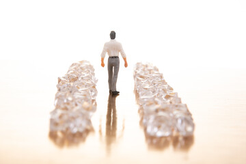 A small businessman walks between gleaming crystal piles on a reflective golden floor, representing...
