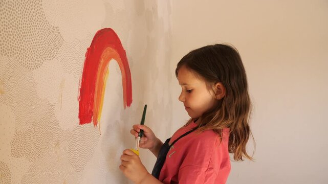 Young girl painting rainbow on wall with brush and tempera colors