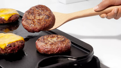 Grilling juicy beef patties on a flat top griddle with melted cheddar cheese in a bright kitchen...