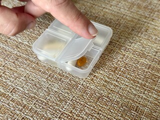 The weekly transparent pill box is designed for convenient and efficient daily storage of dietary supplements and pills. The woman's finger points to the capsule compartment.