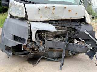 This minibus was significantly damaged as a result of a serious head-on collision. A seriously damaged grey minibus, which shows significant collision marks in the front and extensive rust marks.