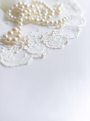 A lustrous strand of classic white pearls gently rests on delicate white lace fabric, creating an elegant and soft texture against a bright, clean white background. Ideal for themes of weddings, luxur
