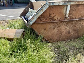An Old and Rusty Dump Container That is Surrounded by Lush, Overgrown Grass and Weeds. A weathered...
