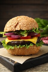 Delicious hamburger with patty and cheese on wooden table, closeup