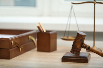 Judge's gavel and scales on wooden table in office, closeup