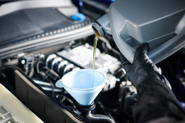 Worker pouring motor oil from canister into car engine, closeup