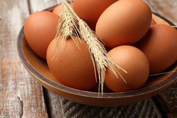 Raw eggs and spikes of wheat on wooden table, closeup
