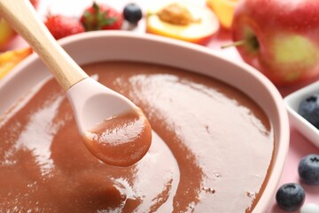 Baby food. Eating tasty puree with spoon at pink table, closeup