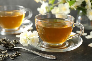 Aromatic jasmine tea, brew and flowers on grey table, closeup
