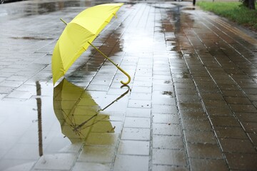 Yellow umbrella on wet asphalt outdoors, space for text