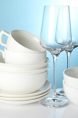 Different clean dishes on white table against light blue background, closeup