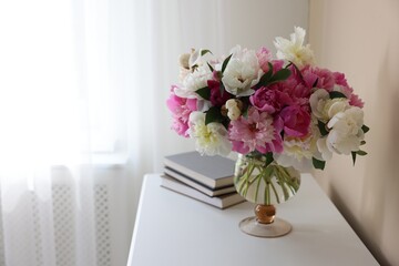 Bouquet of beautiful peonies and books on white table indoors, space for text. Interior design