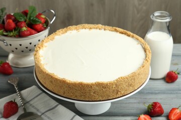 One tasty cheesecake, strawberries and milk on grey table against wooden background, closeup