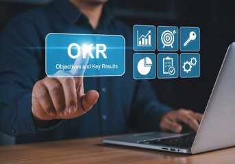 Naklejka premium OKR Objectives, Key and Results concept. Goal setting and tracking results, measuring results with OKRs. Businessman using laptop with OKR icon on virtual screen.