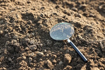 Magnifying glass on dry soil in field, space for text