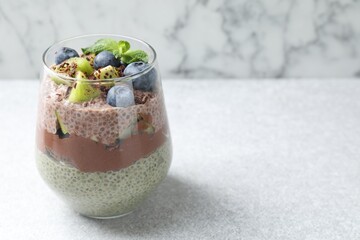 Delicious chocolate pudding with chia seeds, kiwi, mint and blueberries in glass on grey textured table against marble background, closeup. Space for text