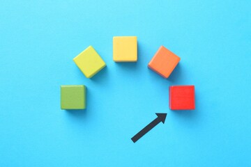 Maximum. Colorful cubes and arrow pointing at red one on light blue background, flat lay