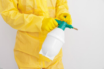 Pest control worker in protective suit spraying insecticide near white wall, closeup