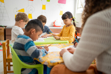 Preschool children sitting at a table coloring with their teacher. Kindergarten art activity encourages creativity, fine motor skills, and learning through play