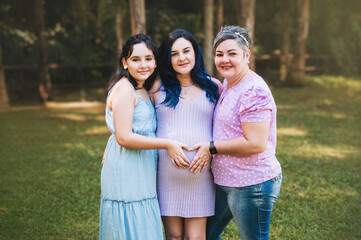 pregnant woman in dress with eldest daughter and grandmother outdoors.