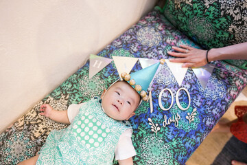 A 100-day-old Japanese baby lies on a colorful sofa while a young mother in her 20s carefully...