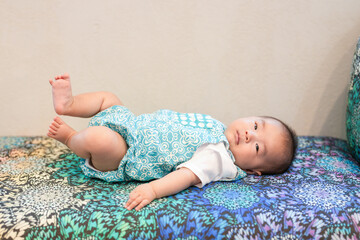 A Japanese baby celebrating their 100th day lies on a colorful sofa, surrounded by cushions. Their...