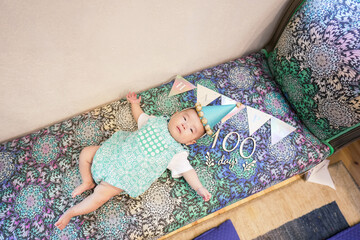 A 100-day-old Japanese baby lies comfortably on a vibrant, colorful sofa, with festive decorations...