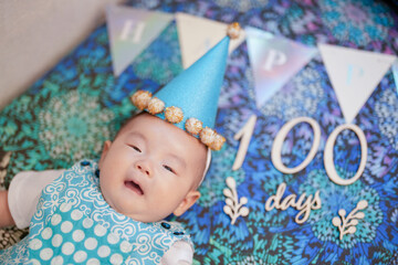 A 100-day-old Japanese baby lies comfortably on a vibrant, colorful sofa, with festive decorations...