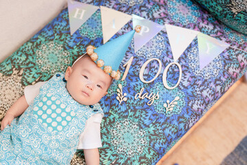 A 100-day-old Japanese baby lies comfortably on a vibrant, colorful sofa, with festive decorations...