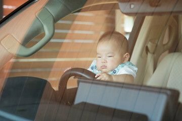 On a sunny day, a Japanese 100-day-old baby sits in the driver's seat of a car parked in the home...