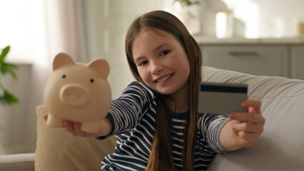 Happy little girl show at camera piggy bank credit debit card banking money finance smiling budget...