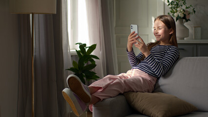 Little girl sitting on sofa mobile phone user smartphone cellphone technology gadget network social...
