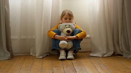 Unhappy little European girl hugging teddy bear toy lonely sad stress divorce worried alone...